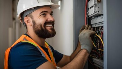 Eletricista Perto de Mim sorrindo e trabalhando no quadro de distribuição.