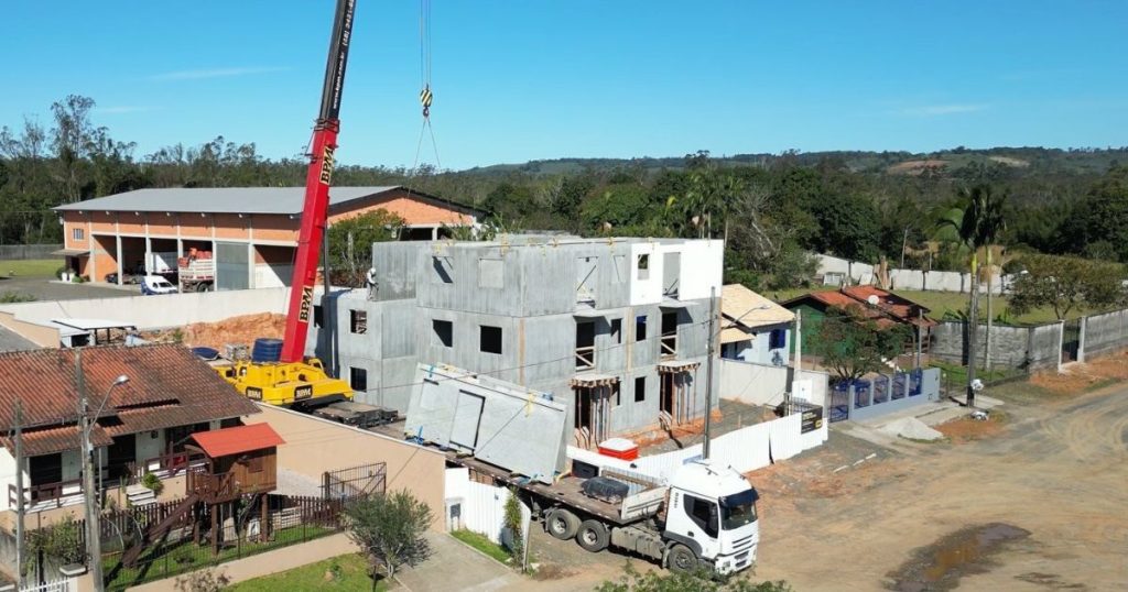 Caminhão e guindaste montando módulos, a logística da Construção Pré-Fabricada.