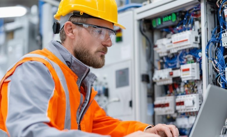 Eletricista testando painel de controle com laptop, foco em segurança e qualidade.