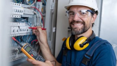 Eletricista Residencial Profissional sorrindo e usando EPI em painel elétrico.